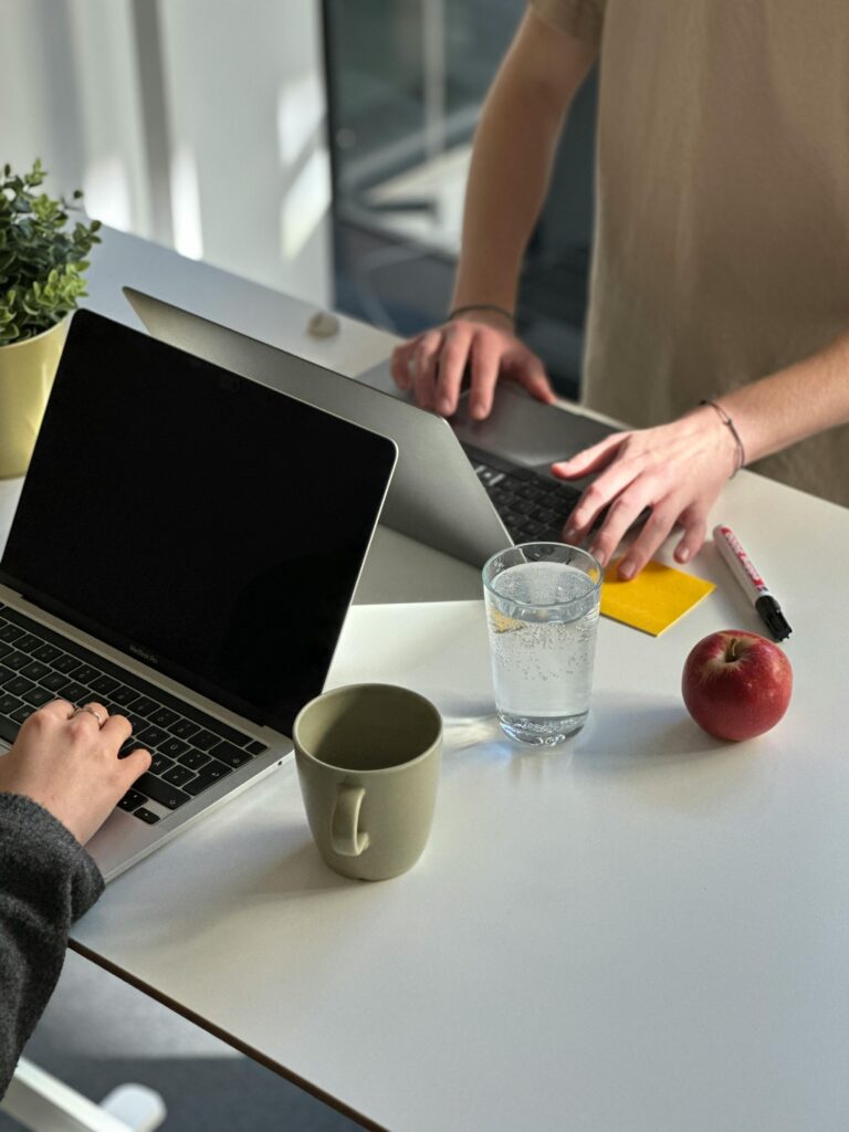 Two people working on laptops at a modern office desk with coffee and an apple.